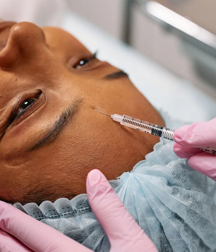Profissional de luvas fazendo uma aplicação no rosto de uma paciente negra