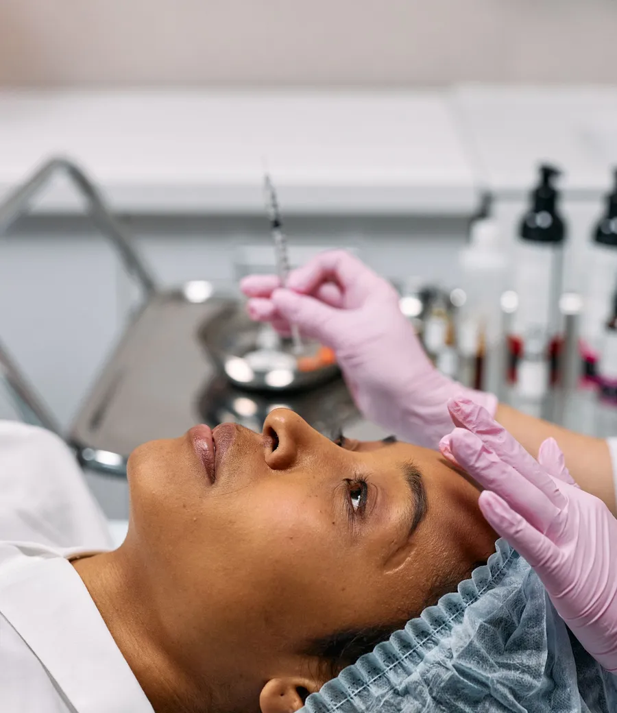 Profissional de luvas segurando uma seringa perto do rosto de uma paciente negra